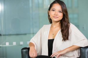 A professional Asian businesswoman sitting confidently in a modern office setting.