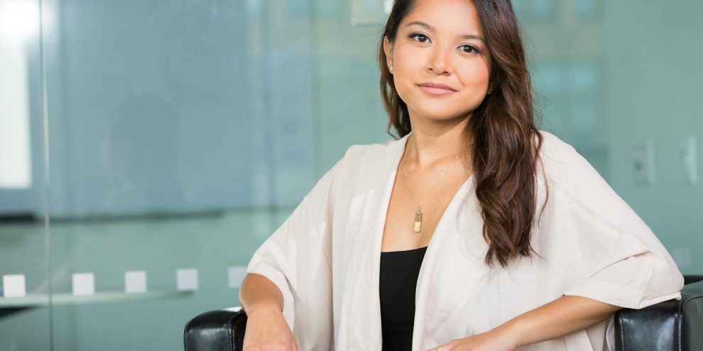 A professional Asian businesswoman sitting confidently in a modern office setting.