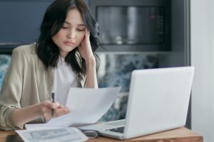 Focused young woman reviewing financial documents with a laptop in a home office setting.