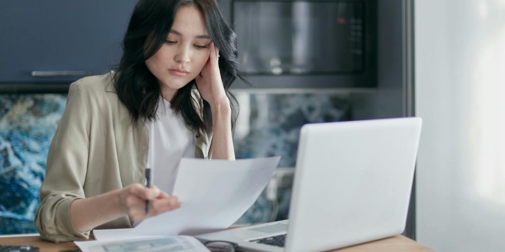Focused young woman reviewing financial documents with a laptop in a home office setting.
